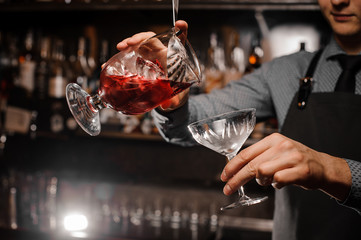 Barman pouring an alcoholic cocktail into the cocktail glass