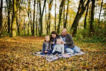 Fototapeta premium Happy caucasian family of mom dad and little girl with boy sitting on plaid at majestic autumn fall forest.