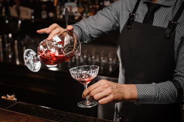 Bartender s hand pouring an alcoholic drink into the cocktail glass
