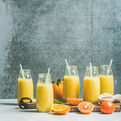 Obraz na płótnie Canvas Healthy yellow smoothie with citrus fruit and ginger in bottles on wooden board over light marble table, selective focus, copy space, square crop. Clean eating, vegan, dieting food concept