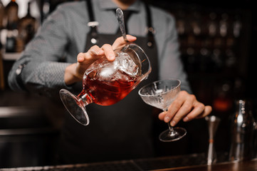 Barman pouring fresh alcoholic drink into the cocktail glass