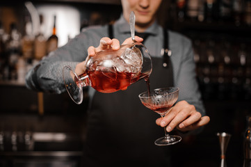 Barman pouring a fresh alcoholic drink into the cocktail glass