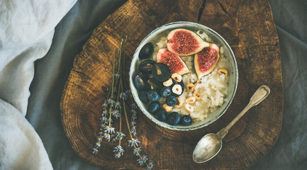 Healthy winter breakfast. Rice coconut porridge with figs, berries and hazelnuts in bowl over rustic wooden board background, top view. Clean eating, vegetarian, vegan, alkiline diet food concept - obrazy, fototapety, plakaty