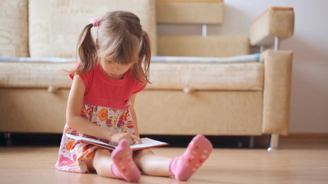 Little girl reads book sitting on the floor