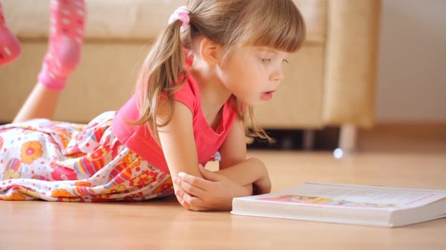 Little girl reads book lying on the floor