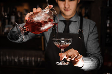 Young male barman pouring a fresh alcoholic cocktail into the cocktail glass