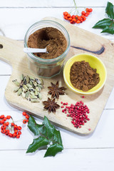 Gingerbread spices in the jar. White, wooden table. Wooden kitchen board.