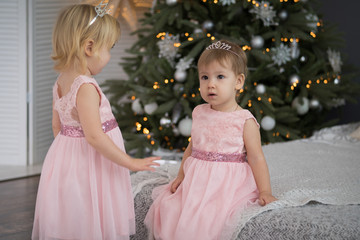 Two little girls in a gown near a Christmas tree at Christmas