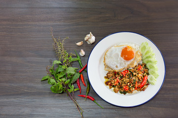 Spicy Stir fried chicken chopping with basil leaves and fried egg Thai food in white dish on wooden table