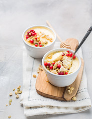 Classic cheesecake in small ceramic jars with fresh cranberries, nuts and honey on light concrete background and wooden board. The most delicious dessert or the perfect healthy breakfast!)