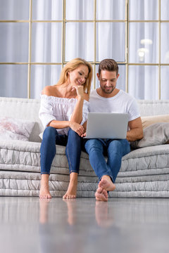 A beautiful young couple sitting on the sofa and using a laptop.