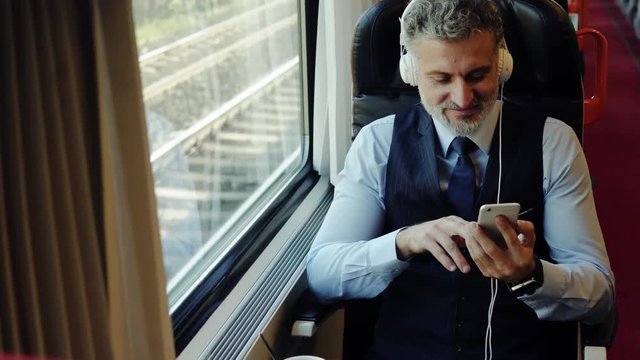 Mature businessman with smartphone travelling by train.