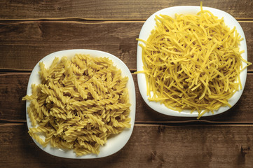 Dry pasta on a plate on a wooden background. A white plate. A series of snapshots of healthy nutrition.