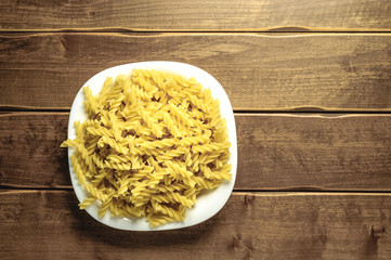 Dry pasta on a plate on a wooden background. A white plate. A series of snapshots of healthy nutrition.