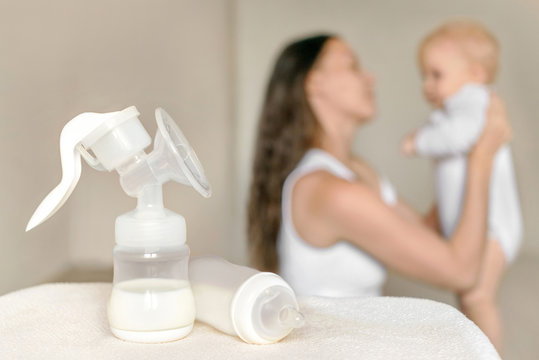 Manual breast pump and bottle with breast milk on the background of mother holding baby in her hands. Maternity and baby care.