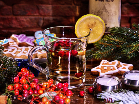 Christmas Tea cup glass and multicolored cookies on form stars on plate with fir branches. Mug decoration lemon slice on wooden table. Xmas treats and candels. Bottle of wine in background.
