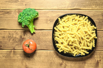 Dry pasta on a plate on a wooden background. A black plate. A series of snapshots of healthy nutrition.