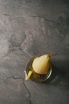Traditional dessert poached pear in white wine served in glass bowl with syrup and lemon zest over gray texture table. Top view with space