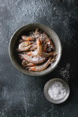 Raw whole fresh uncooked prawns shrimps on ice on vintage metal tray with plate of sea salt over black texture background. Top view with space