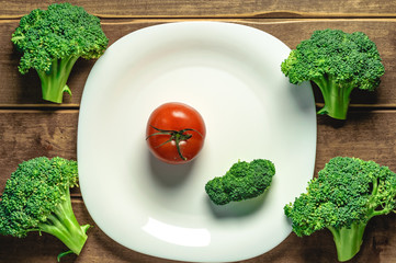 Tomato and broccoli on a plate on a wooden background. A white plate. A series of snapshots of...