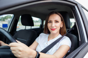 Young woman in white shirt driving car on the road. Hispanic girl steering wheel in auto