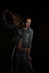 Fashionable brunette woman in trendy jeans jacket posing at black background