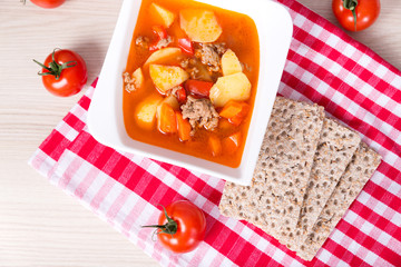 Fototapeta na wymiar goulash soup with tomato, potato, paprika on wooden background
