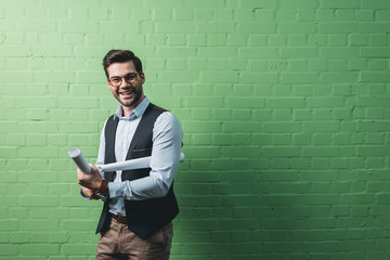 young handsome businessman with blueprints in front of green wall