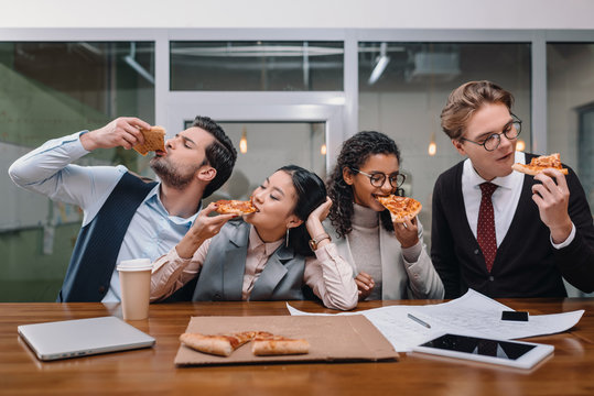 cheerful multiethnic businesspeople eating pizza in office - Powered by Adobe