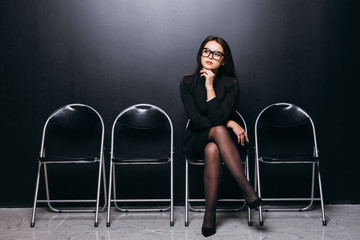 Waiting in line. Confident young businesswoman sitting on chair against black background