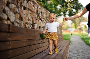 Pretty little girl walking on the bench with help of mother s hand