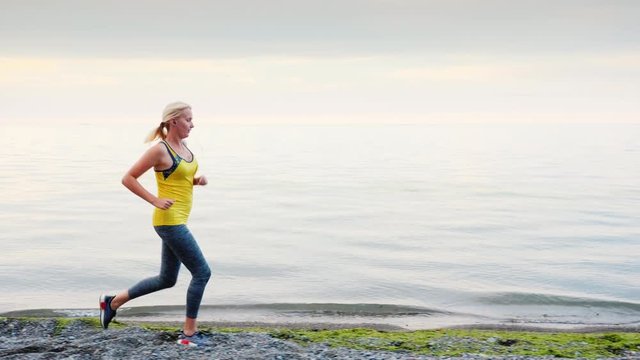 A woman in a yellow T-shirt runs along the shore of a lake or sea