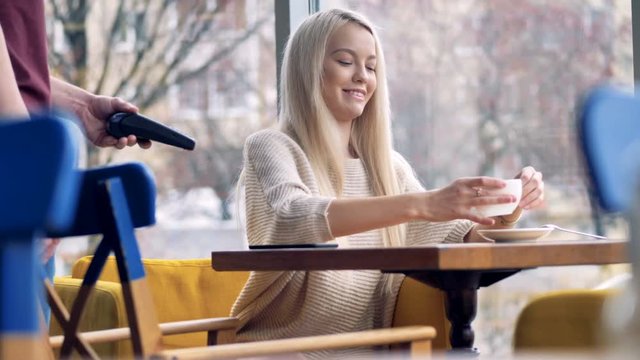 A girl stops drinking her coffee to make a NFC payment. 