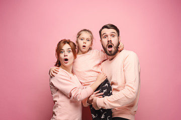 Surprised young family looking at camera on pink