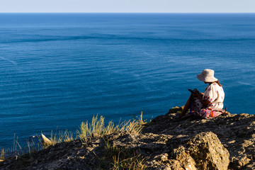 Fototapeta na wymiar Girl sits on the edge of a cliff and looks at the sea
