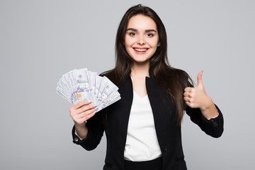 Smiling business woman holding money with thumbs up over gray background