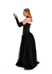 Fototapeta premium full length portrait of a blonde girl wearing black gothic gown. standing pose, isolated on white background.