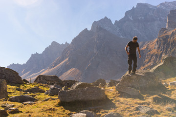 Young adult man hiker climb down a rock on mountain in sunny autumn day on Alps in Italy outdoor.