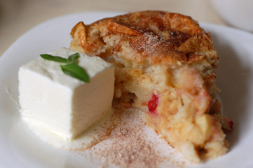 Piece of apple pie with a cube of white milk ice cream and mint leaves on the plate.