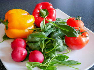 Fresh green vegetable salad with radish, tomatoes, color peppers on the white plate.