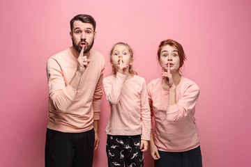 Surprised young family looking at camera on pink