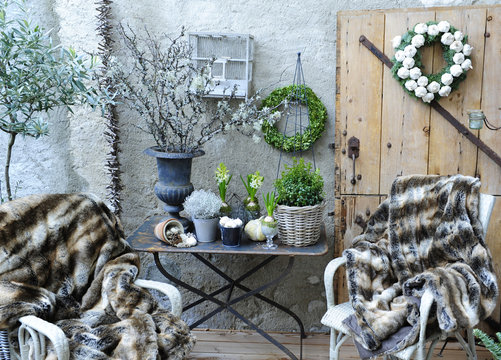 Terrasse et son atmosphère hivernale avec chaises en osier, plaid en fausses fourrures, buis, et branches séchées
