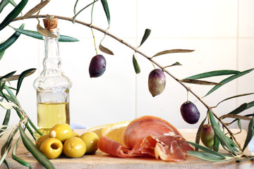 A bottle with olive oil, an olive branch and a light breakfast from stuffed olives and a jamon.
