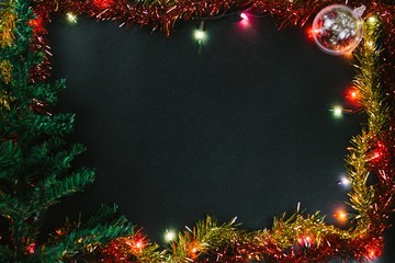Christmas and New Year Decoration Background with Multi-Color Small Light Bulb, Christmas Tree, Gold and Red Tinsel, and Ball on a Black Background