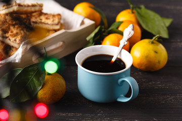 Cup of tea and branch with Christmas lights on background.