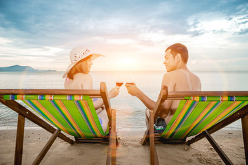Asian couple walking on the beach when the sun is about to sunset during the honeymoon. There are  Couple walking on Valentine's Day and drinking the wine.