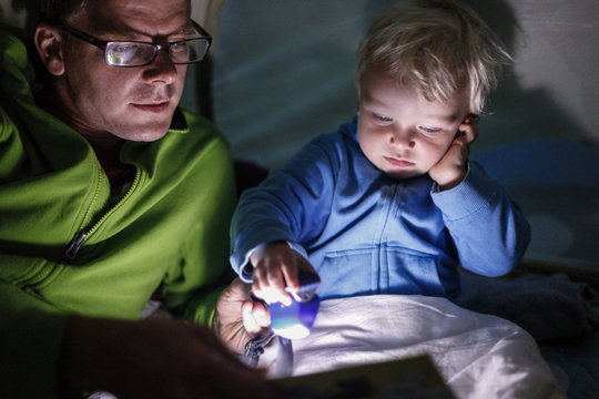 Father reading his son (2 years) from a book inside a tent, Haide, Ummanz, Island of Ruegen, Mecklenburg-Western Pomerania, Germany