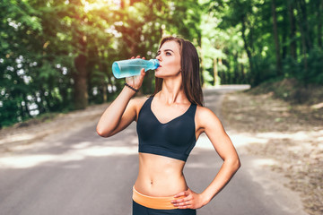 Young fitness girl drinking water in the park