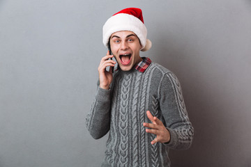 Emotional man wearing christmas santa hat talking by phone.