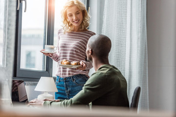 girlfriend brought cup of coffee and croissants for african american boyfriend that working at home